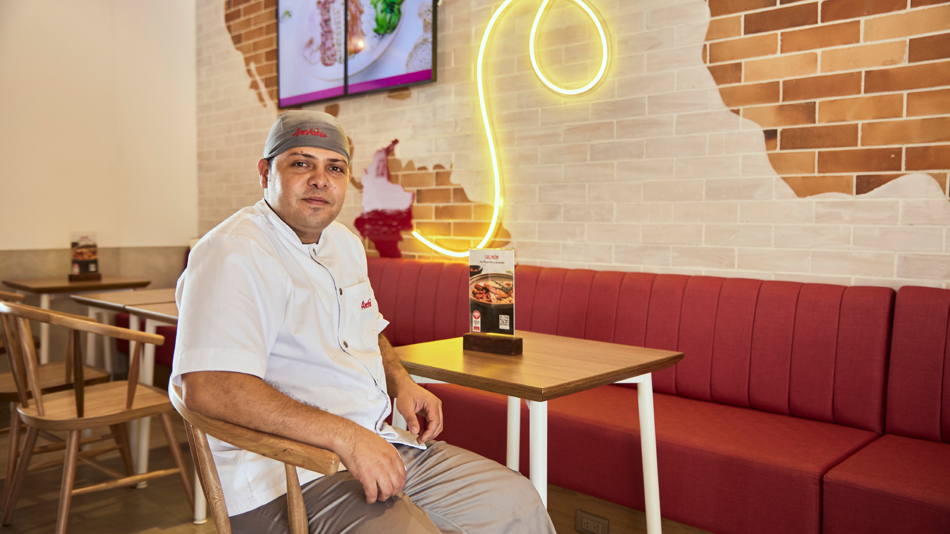 Archies chef in white uniform standing in restaurant with brick wall and neon sign